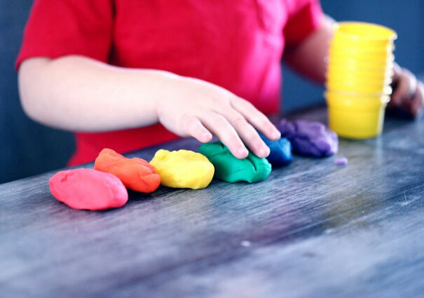 Child arranging colored clay on a table, displaying creativity and playfulness.