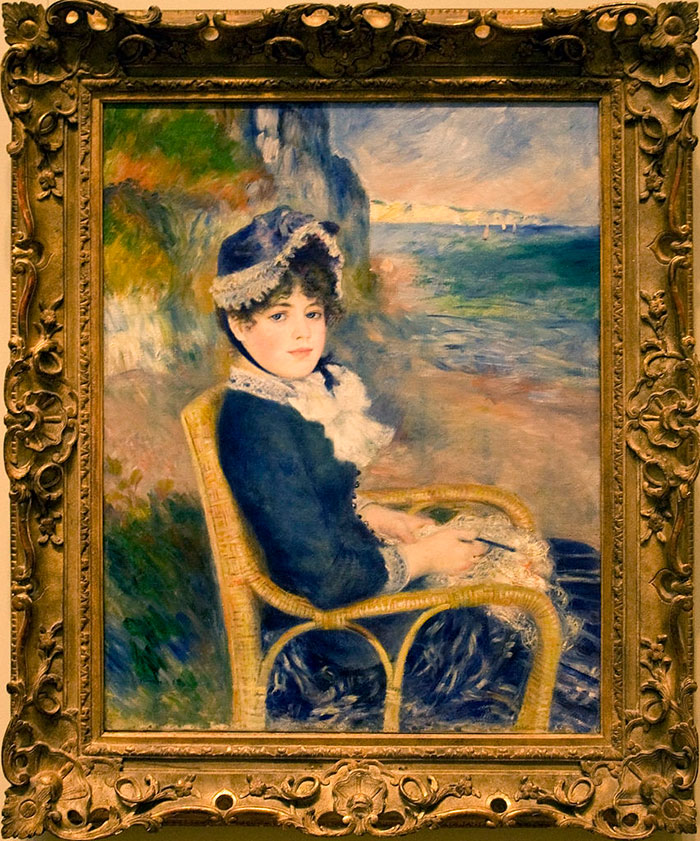 Famous painting of a woman seated by the sea, wearing a blue dress and hat, framed in ornate gold.