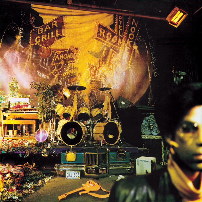 Vibrant and iconic album cover with a drum set, colorful neon signs, and scattered instruments.