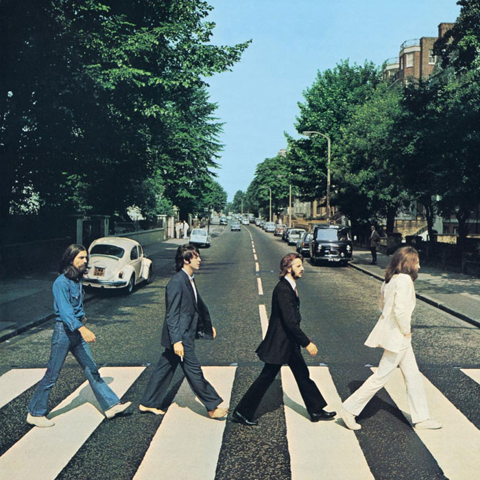 Iconic album cover featuring four men walking across a zebra crossing on a street lined with trees and cars.