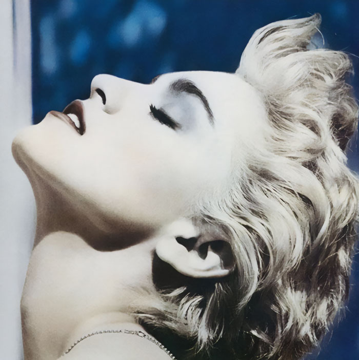 Close-up portrait of a blond person with bold makeup, head tilted back, from a famous album cover.