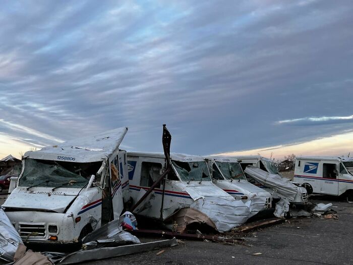 Damaged USPS mail trucks in Mayfield aftermath, showcasing tornado destruction under a cloudy sky. Damaged USPS mail trucks in Mayfield aftermath, showcasing tornado destruction under a cloudy sky.