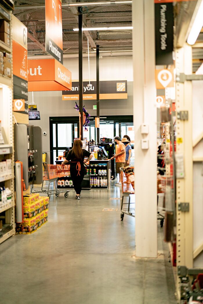 Customers and staff in a busy hardware store aisle near plumbing and checkout sections during a typical day.