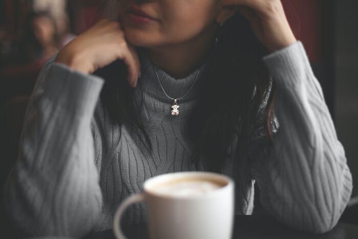 Woman in a gray sweater sitting at a table with a coffee cup, reflecting on a date that took a weird or disturbing turn