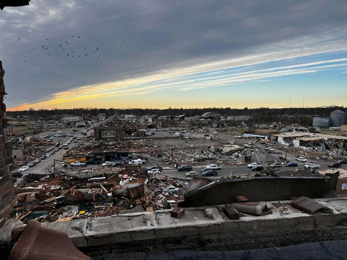 A wide view of Mayfield tornado aftermath showing extensive destruction and debris under a cloudy sky at sunset. A wide view of Mayfield tornado aftermath showing extensive destruction and debris under a cloudy sky at sunset.