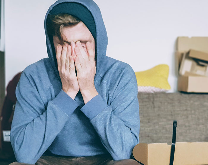 man covering face with both hands while sitting on sofa