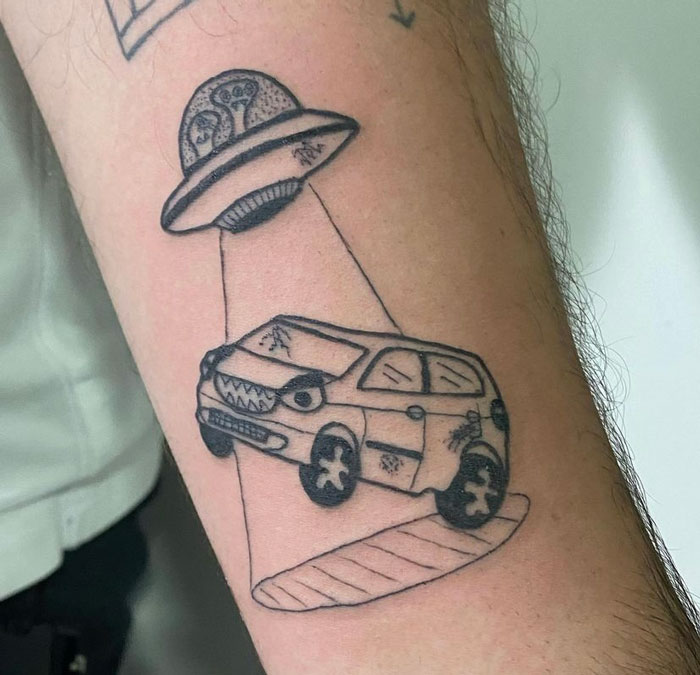 Tattoo of a UFO beaming up a car with quirky, intentionally rough design elements on a person's arm.