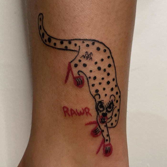 Quirky leopard tattoo design with "RAWR" text on leg; simple art by tattoo artist known for unique, non-traditional style.