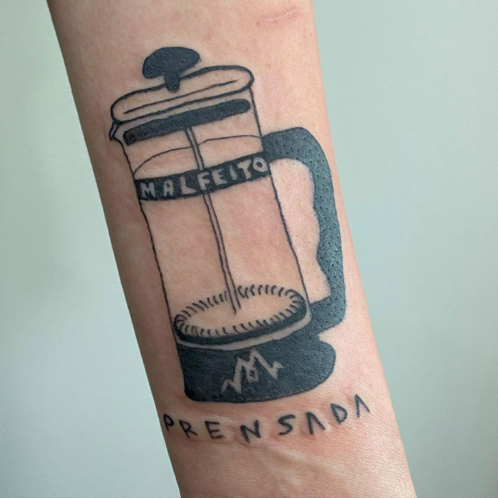 Tattoo of a French press with unique design on arm, showcasing artist's charmingly imperfect drawing style.