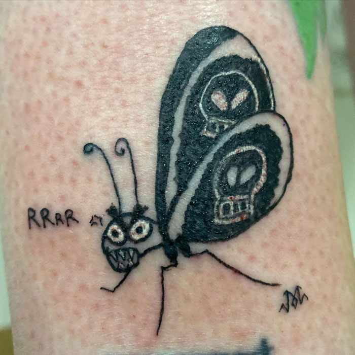 Whimsical tattoo of a butterfly with skull wings and the text "RRAR," showcasing unique artistic style.