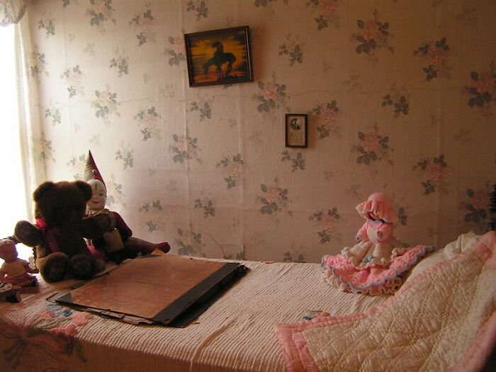 Vintage bedroom with stuffed toys on bed, old wallpaper, and worn book hinting at parents' hidden secrets awareness.