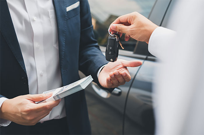 Handshake between two business professionals exchanging car keys and cash, revealing secrets large corporations hide from customers.