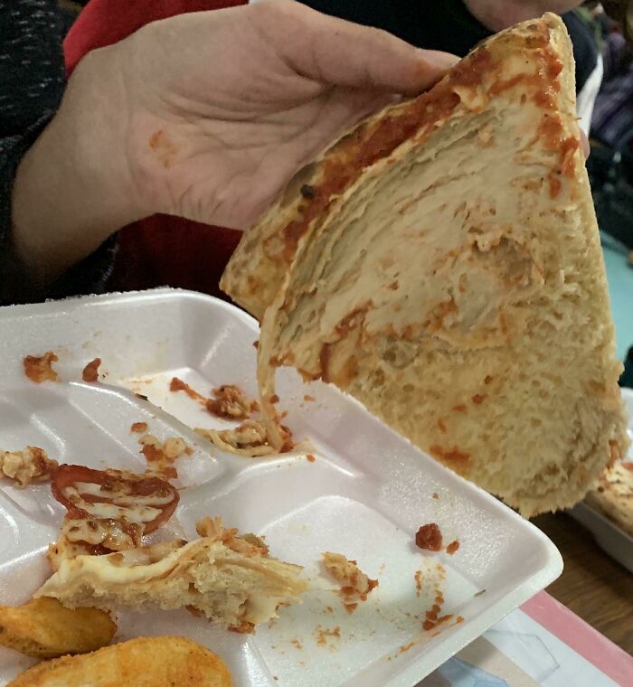 Hand holding a folded slice of pizza with sauce and cheese in a divided tray, school lunches from around the world.