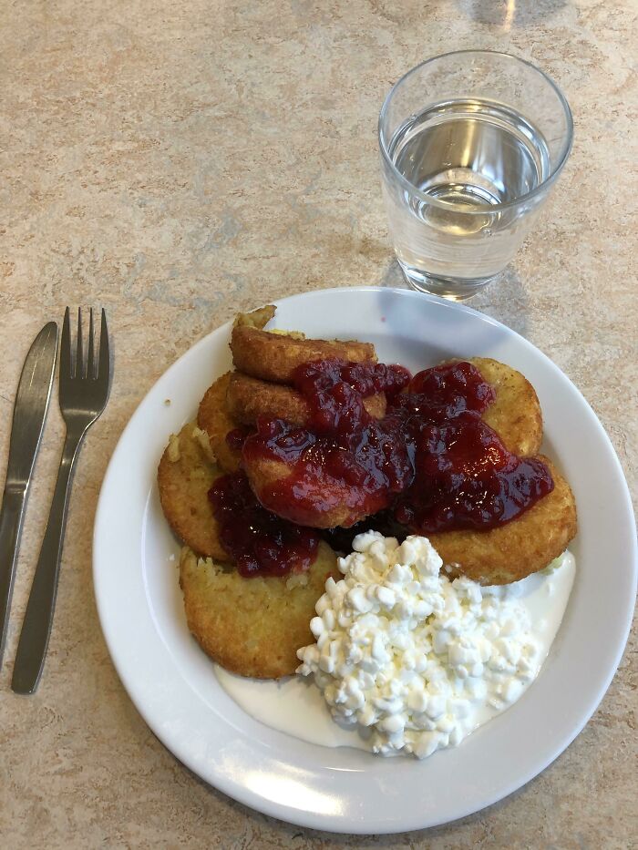 Plate of crispy potato patties topped with red berry sauce and cottage cheese, served with a glass of water, school lunches photo.