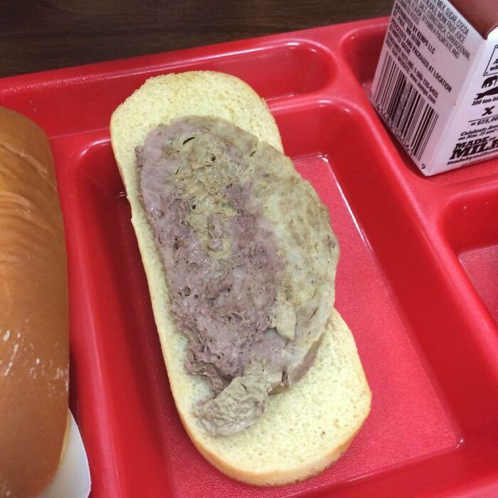 School lunch featuring a plain sandwich with processed meat slice on a red tray alongside a carton of milk.