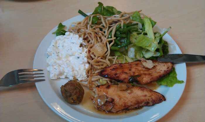 Plate of school lunches featuring grilled chicken, noodles, cottage cheese, salad, and a fried side from around the world.