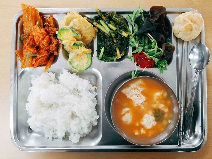 School lunches tray with rice, soup, kimchi, vegetables, and a bread roll showcasing diverse school lunches from around the world.