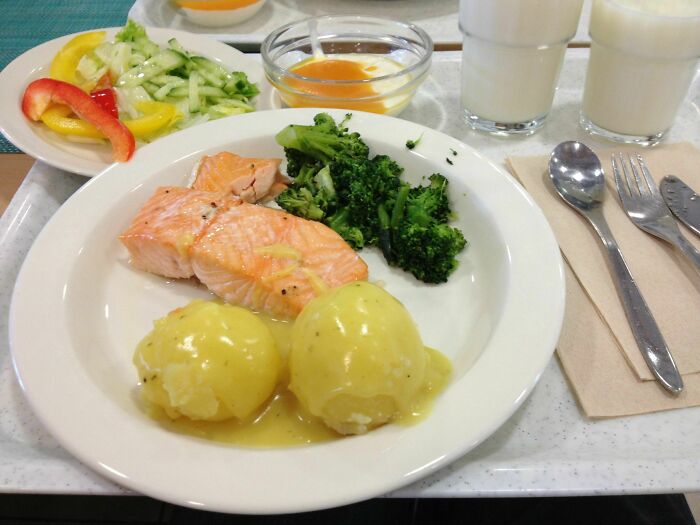 School lunch featuring salmon, boiled potatoes with sauce, steamed broccoli, salad, and milk on a tray showcasing school lunches.