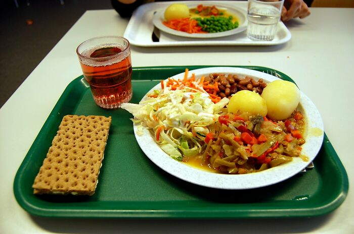 School lunch tray with boiled potatoes, mixed vegetables, beans, salad, crispbread, and a glass of juice.