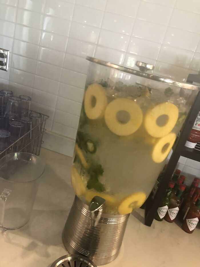 Large beverage dispenser with lemon slices and herbs, part of school lunches from around the world.