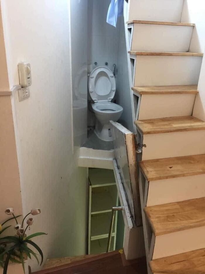 Unusual home interior with toilet awkwardly placed under a staircase.