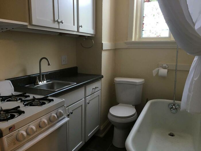 Awful home interior with a cramped kitchen and bathroom setup, featuring a stove, sink, toilet, and bathtub in one space.