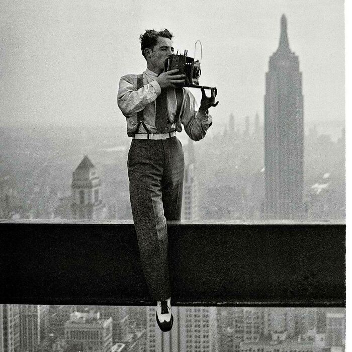 Man with camera on skyscraper beam, capturing iconic historical photo in New York City skyline.