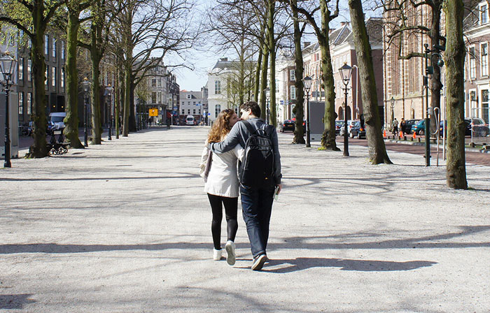 Couple walking down a tree-lined path in a quiet city street, reflecting on hidden secrets parents may have.
