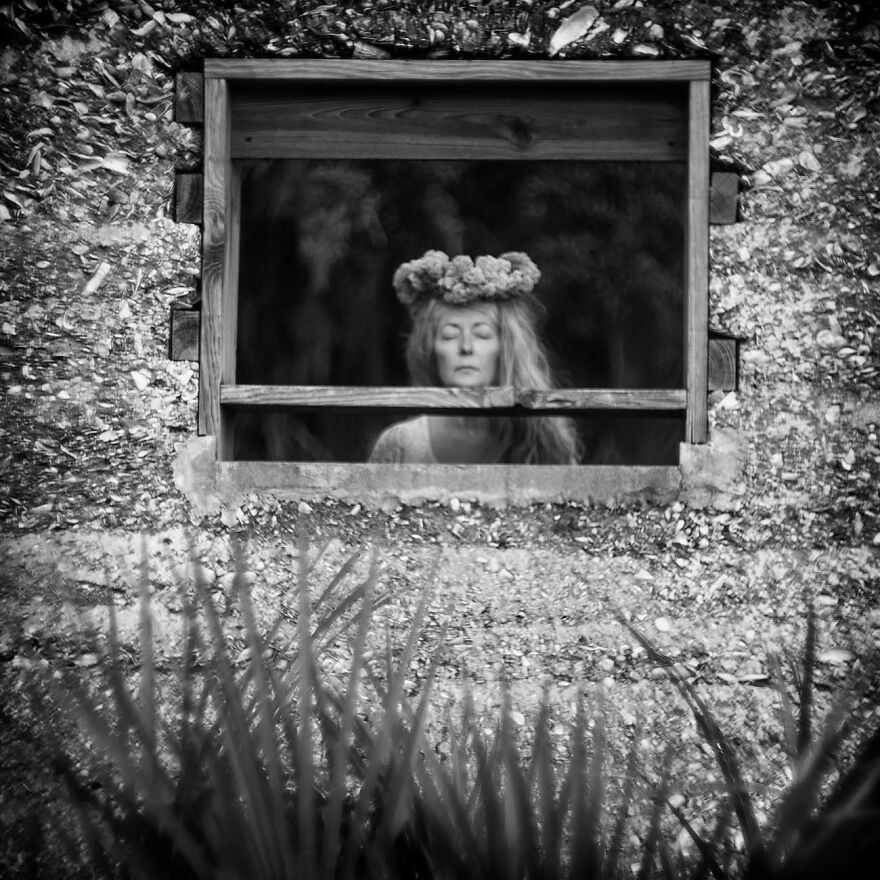 Woman with a flower crown framed by a rustic window in a black and white photo, capturing beautiful women around the world.