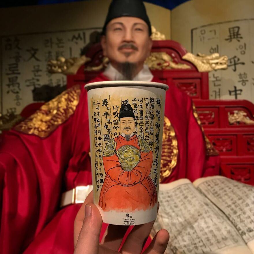 Hand holding a paper cup with detailed illustration of an Asian man in traditional attire, matching background scene.