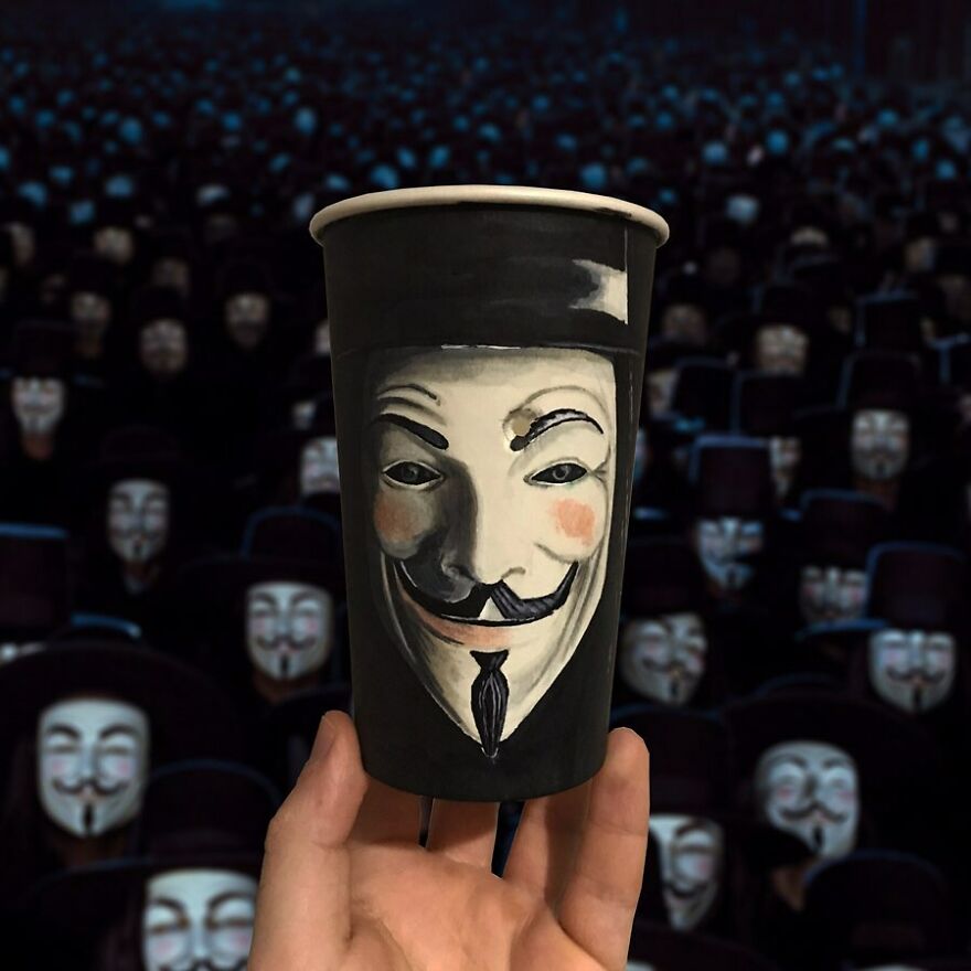 Paper cup illustration of a Guy Fawkes mask held up with many similar illustrated paper cups in the background.