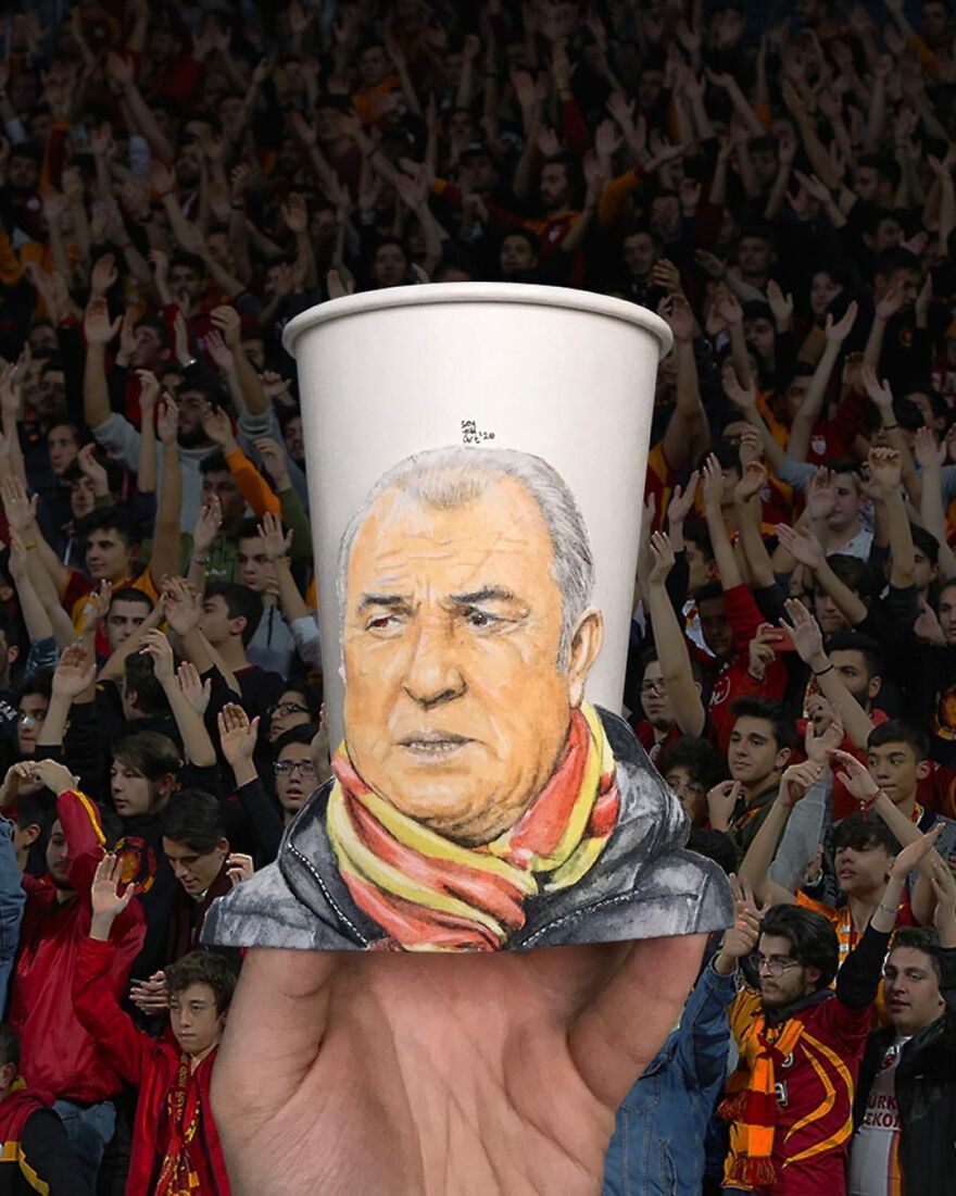 Hand holding a paper cup with a detailed portrait illustration drawn on it among a cheering crowd.