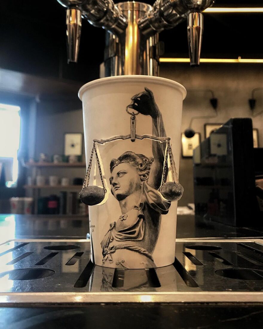 Paper cup with detailed black and white illustration of Lady Justice, showcasing unique art drawn on paper cups while traveling.