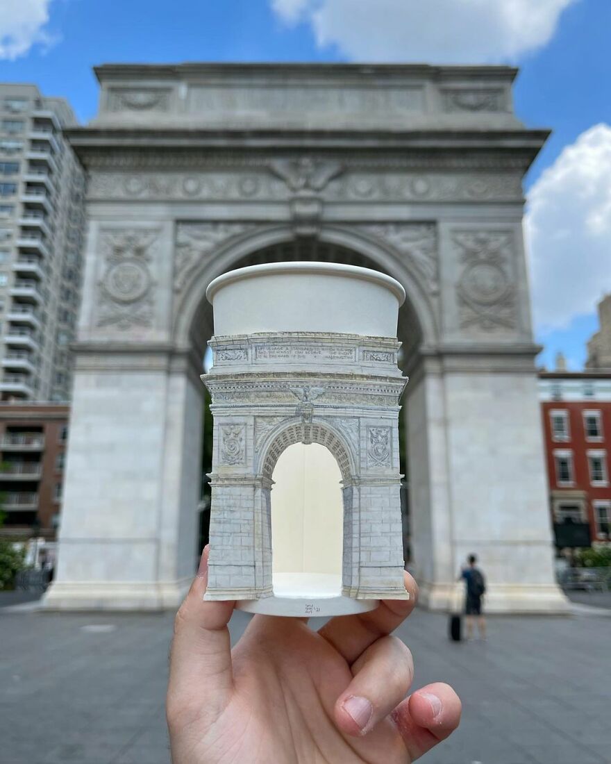 Hand holding paper cup with detailed illustration of arch monument, blending with the real arch in the background during travel.