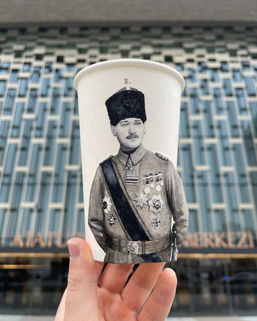 Hand holding a paper cup featuring a detailed black and white illustration of a historical figure in military attire.