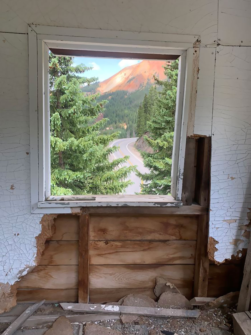 View of beautiful scenery through a window, showcasing a winding road and lush green trees against a mountain backdrop.