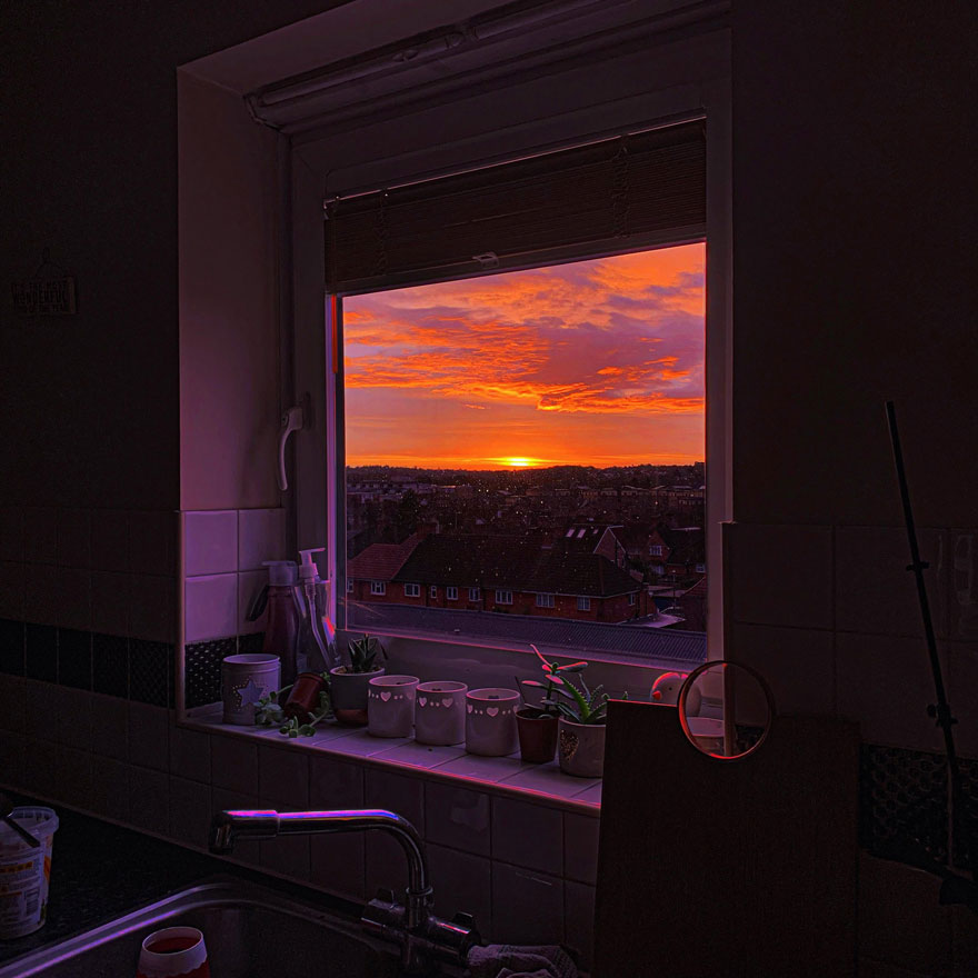 Beautiful scenery of a vibrant sunset through a window, framed by potted plants on the windowsill.