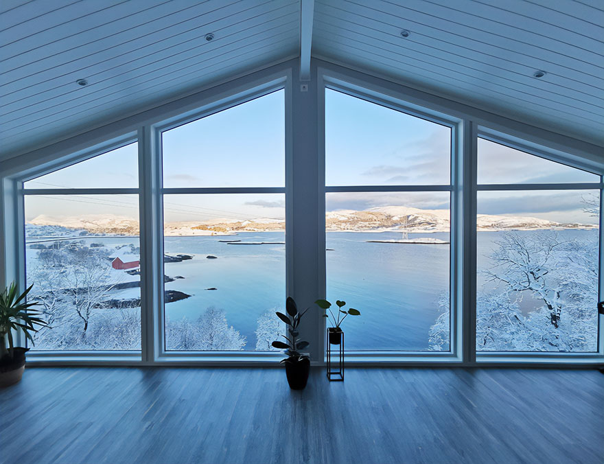Beautiful scenery captured through large windows overlooking a snowy landscape and serene water view.