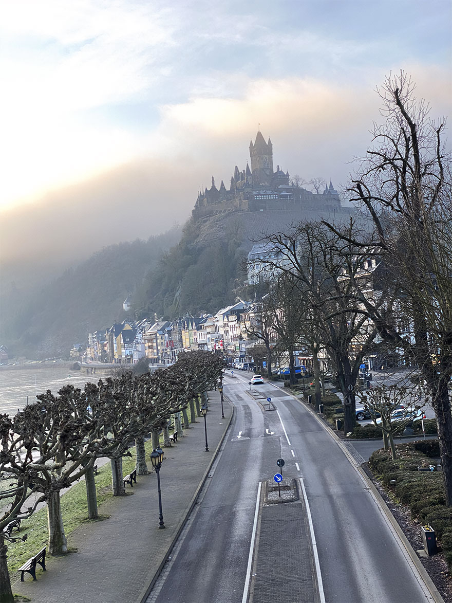 Beautiful scenery with a castle on a hill, overlooking a quiet road and colorful buildings on a misty day.