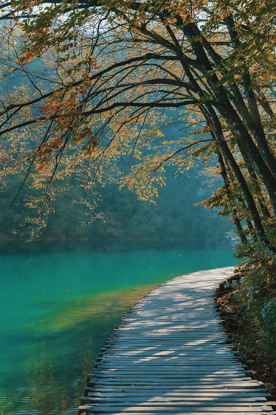 Beautiful scenery with autumn trees and a wooden path beside a serene turquoise lake.