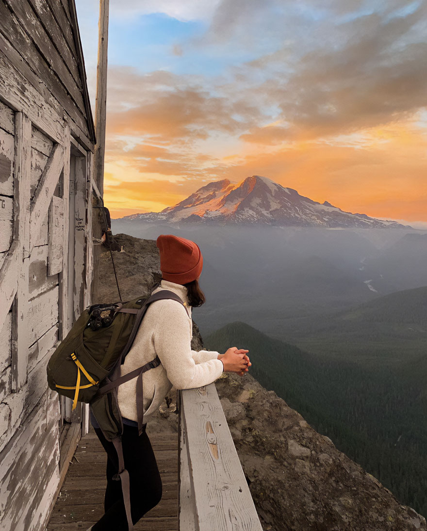 Person in a beanie admires stunning mountain scenery at sunset from a wooden deck, capturing nature's beauty.