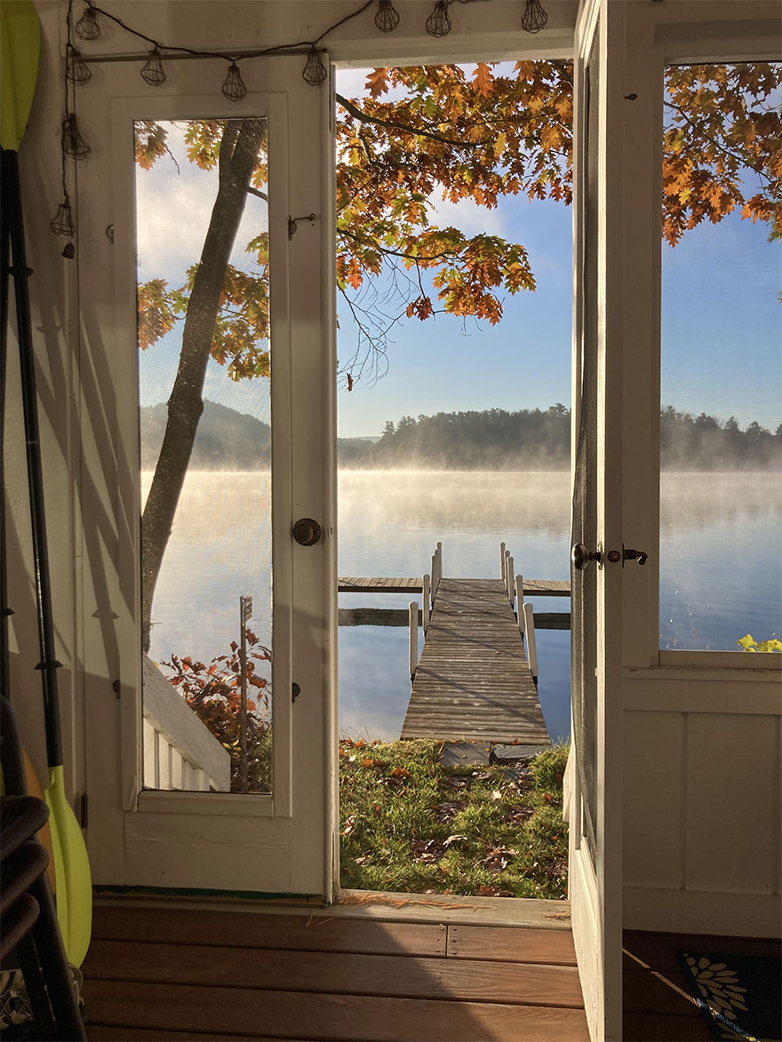 Beautiful scenery of a serene lakeside view from a doorway, with autumn leaves and a wooden dock.
