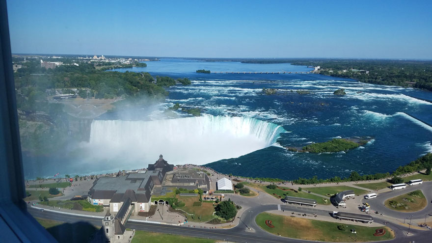 A breathtaking view of a massive waterfall cascading into a river, surrounded by greenery and buildings nearby.