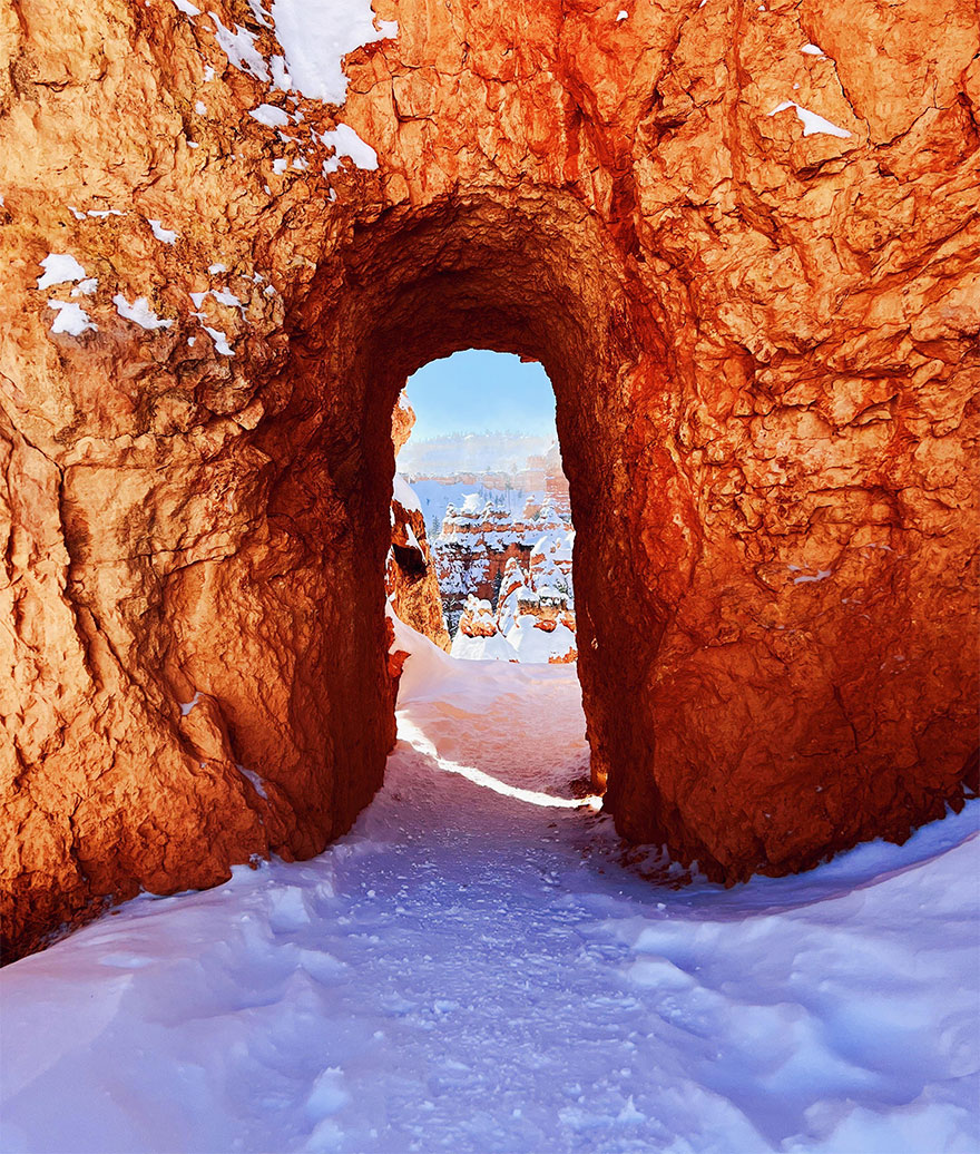 Snowy path through red rocky arch reveals stunning winter scenery.