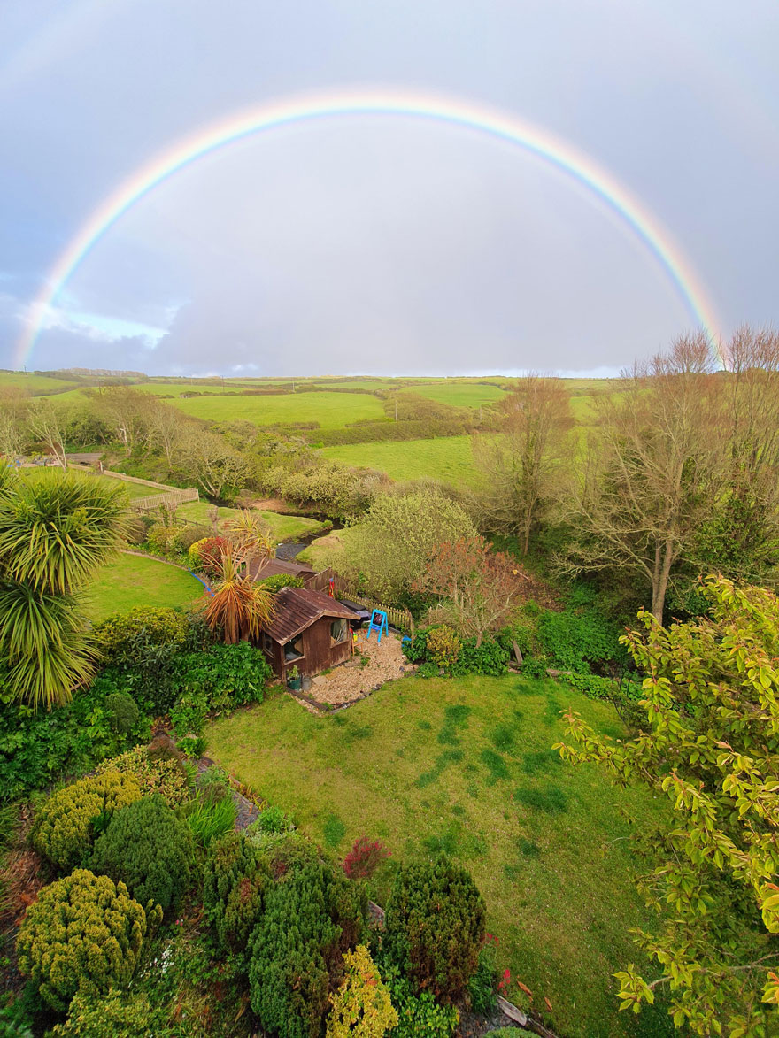 Beautiful scenery of a lush garden beneath a vibrant rainbow arcing across a cloudy sky.