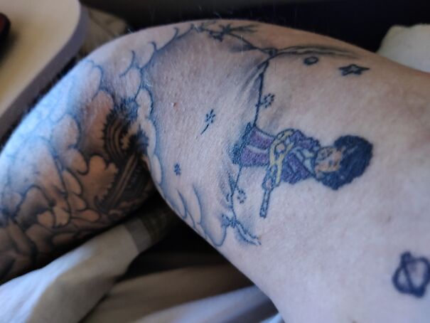 Tattoo featuring a small figure playing guitar, surrounded by clouds and stars.