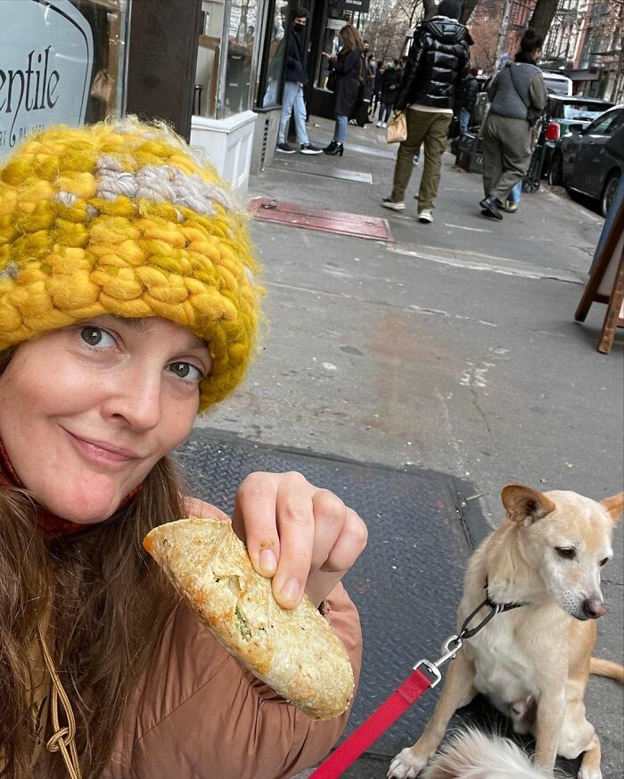 Woman in a yellow knit hat holding food on a city sidewalk with a dog on a red leash in the background, career revival theme.