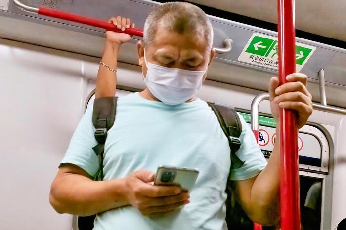 Man wearing mask and backpack holding phone on crowded subway, a lucky accident captured by photographer Edas Wong