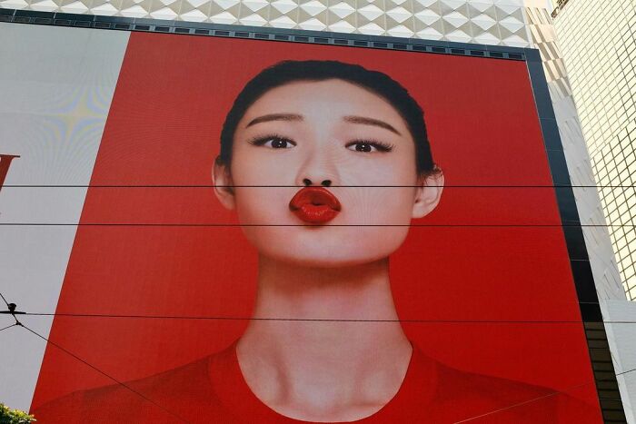 Large outdoor advertisement featuring a woman with red lips against a red background, illustrating lucky accidents captured by photographer.