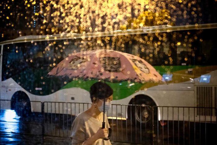 Person with pink umbrella walking in rain at night, raindrops glistening on glass, a lucky accident captured by photographer Edas Wong.